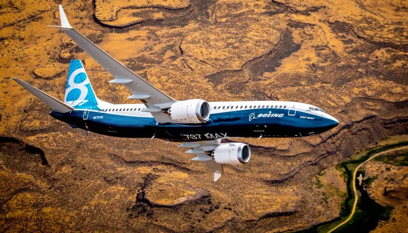 Boeing 737 MAX 8-200 z niebieskim ogonem z cyfrą 8 leci nad pustynnym krajobrazem.