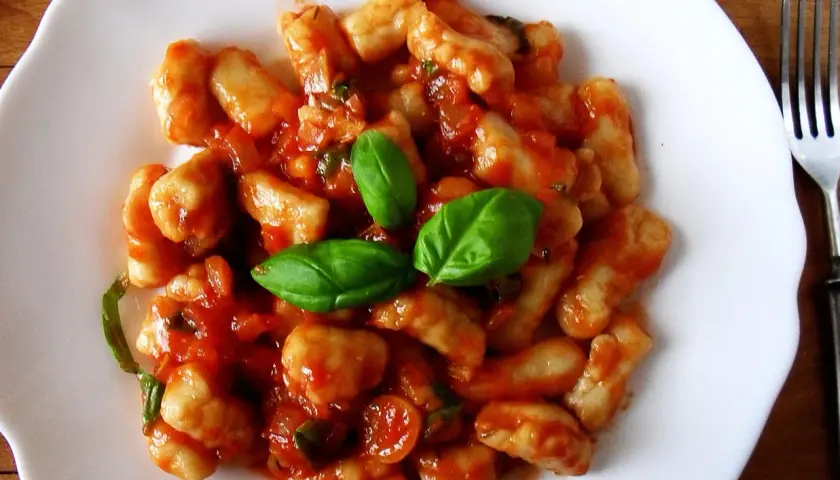 Pyszne gnocchi z sosem pomidorowym i świeżą bazylią na białym talerzu.