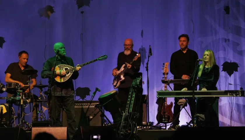 Zespół Dead Can Dance na koncercie. Muzycy grają na instrumentach, w tle fioletowa kurtyna z liśćmi.