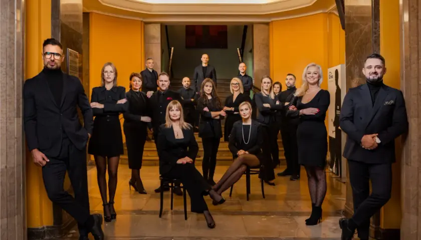 Grupa profesjonalistów w eleganckich czarnych strojach pozuje w holu.
