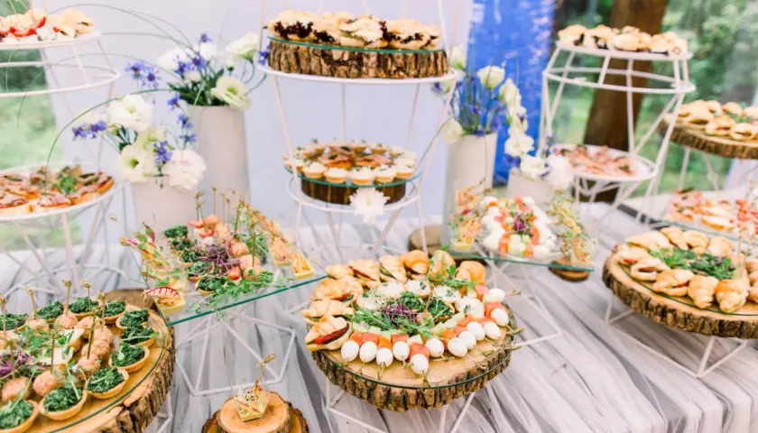 Un buffet de mariage participatif avec une variété de petits fours, tartines et brochettes, joliment présentés sur des rondins de bois et des étagères en verre.