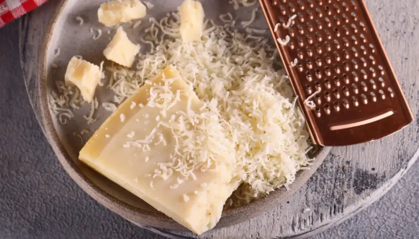 Parmezan na keto: świeżo starty ser i kawałki parmezanu na talerzu obok tarki. Idealny dodatek do keto posiłków.