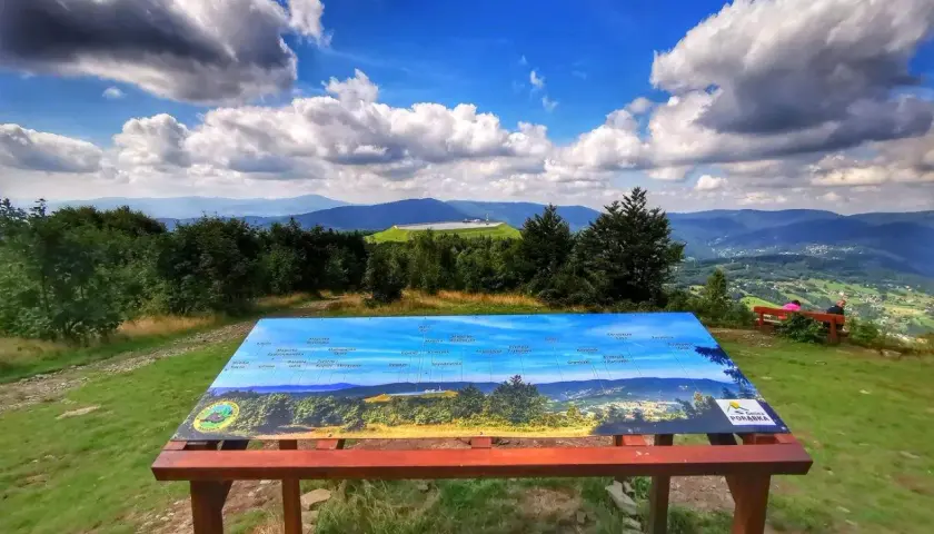 Widok z kiczera szlak na malowniczą panoramę Beskidu Sądeckiego. Tablica informacyjna pomaga zidentyfikować szczyty i miejscowości.