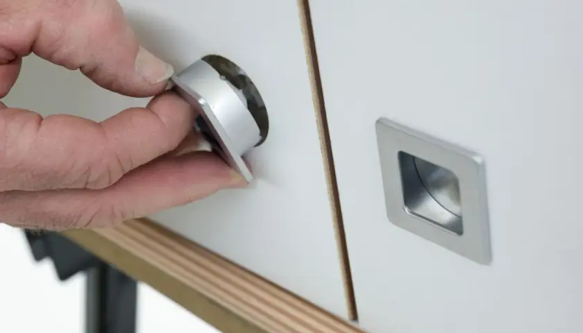 Mano insertando un tirador moderno en un mueble, renovando su aspecto. Ideal para cambiar tiradores mueble antiguo.