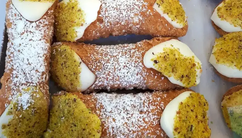 Chrupiące rurki z kremem i pistacjami, posypane cukrem pudrem. Pyszne cannoli kuszą swoim wyglądem.