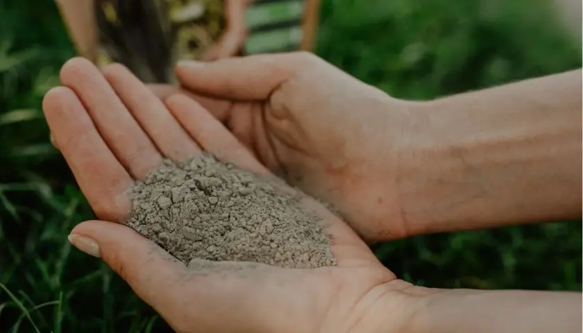 Dłonie trzymające mączkę bazaltową, która jest naturalnym nawozem. Jej zastosowanie to poprawa struktury gleby i dostarczenie roślinom cennych minerałów.