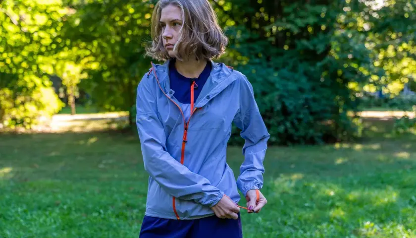 Kobieta w niebieskiej kurtce sportowej z pomarańczowymi zamkami. Taka membrana 10000 co to znaczy? To dobra ochrona przed deszczem i wiatrem podczas biegania.