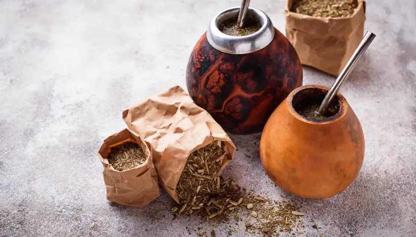 Dwa tykwy z yerba mate i bombillami, obok papierowe torebki z suszem. Czy yerbę można słodzić? To zależy od preferencji!