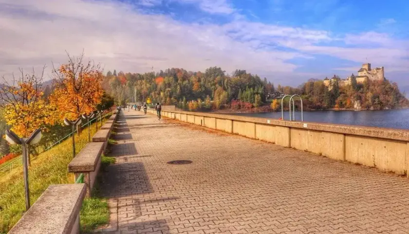 Jesień nad zalewem w Czorsztynie. Spacerowicze i rowerzyści cieszą się widokiem zamku na wzgórzu.