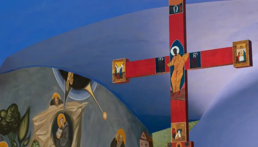 Czerwony krzyż z ikonami i malowidła ścienne przedstawiające sceny religijne, tworzące atmosferę sakralną.