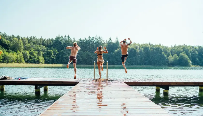 Drei Freunde springen von einem Steg in den See der Mecklenburgischen Seenplatte. Ein perfekter Sommertag am mecklenburgische seenplatte strand.