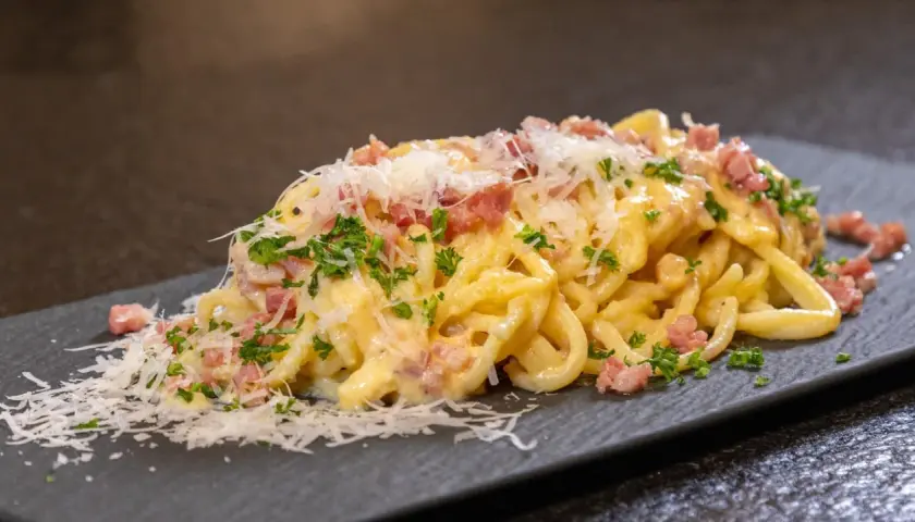 Eine Portion echte Carbonara mit cremiger Sauce, Guanciale und frisch geriebenem Parmesan auf einem dunklen Teller.