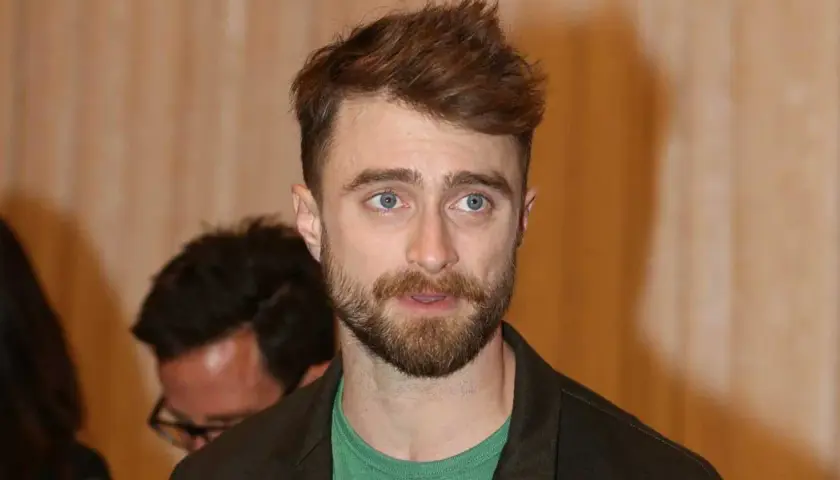 Daniel Radcliffe z zarostem i niebieskimi oczami, jego spojrzenie sugeruje troskę o zdrowie, być może związaną z jego chorobą.