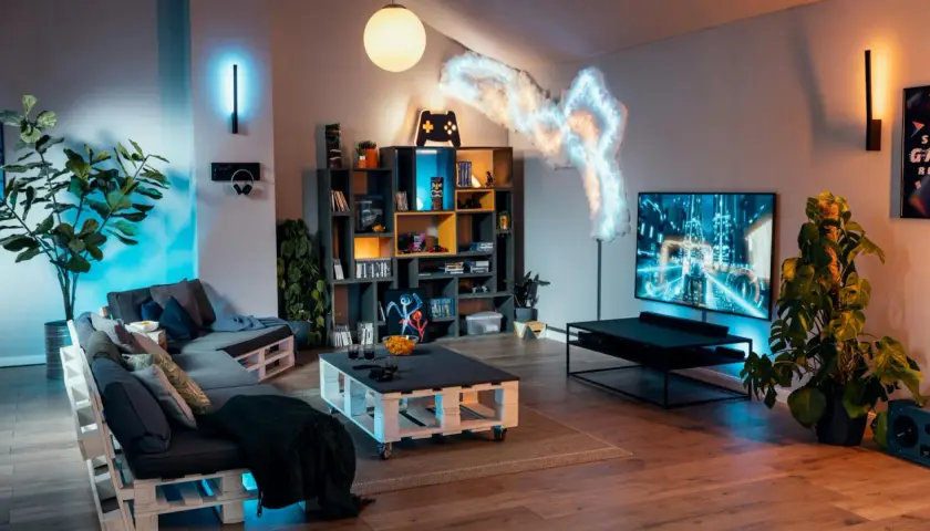 Gemütlicher hobbyraum einrichten mit Paletten-Sofa, Gaming-Regal, großer TV und stimmungsvoller Beleuchtung.