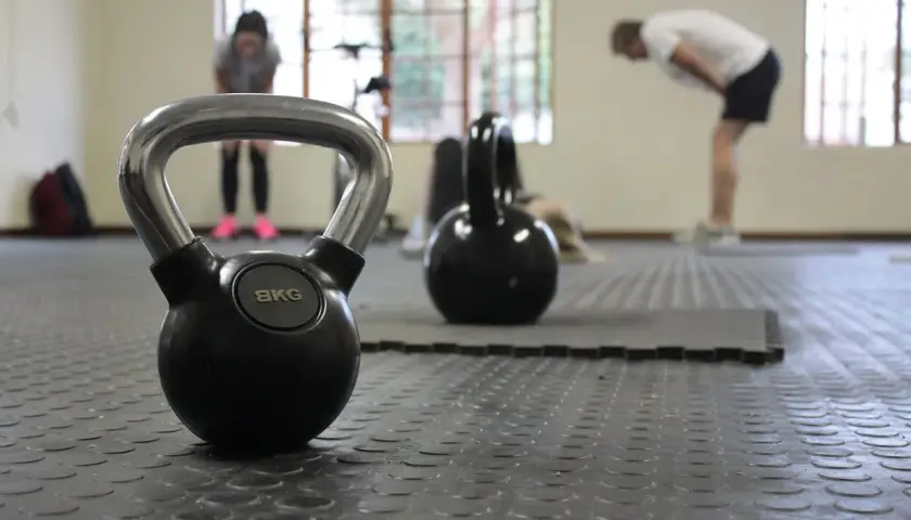 Kettlebell 8kg na siłowni, w tle ćwiczący ludzie.