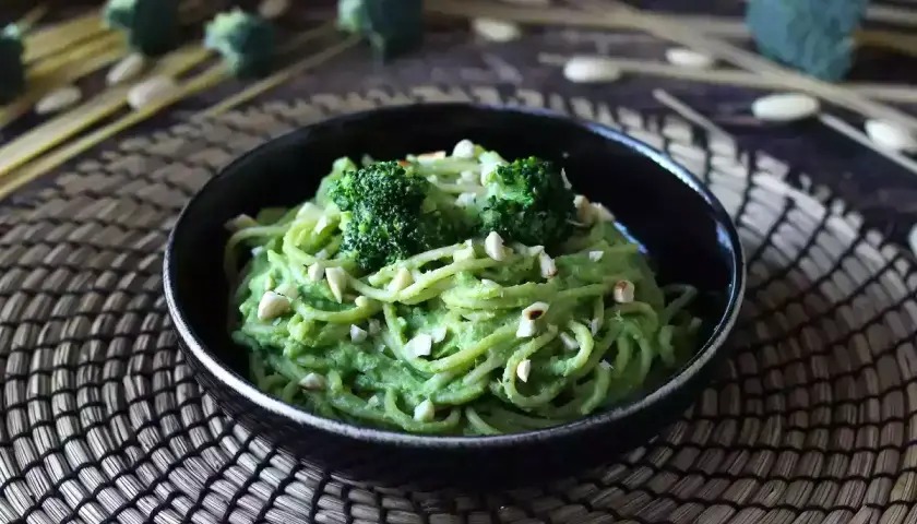 En skål med krämig broccoli pasta, toppad med broccolibuketter och hackade nötter. En härlig och grön måltid.