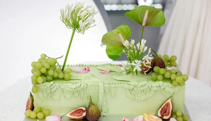 Elegancki tort ślubny w pastelowej zieleni, ozdobiony winogronami, figami i białymi kwiatami.