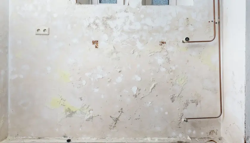 Feuchte Wand mit abblätterndem Putz, Salpeter-Ausblühungen und Kupferrohren. Was ist Salpeter? Ein Salz, das bei Feuchtigkeit entsteht.