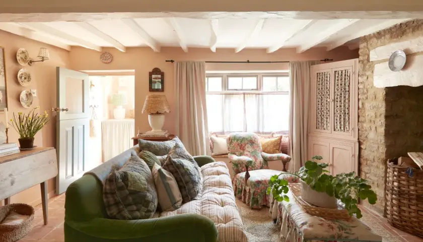 Cozy living room with a green sofa, floral armchair, and charming granny decor. Exposed beams and stone accents add rustic warmth.