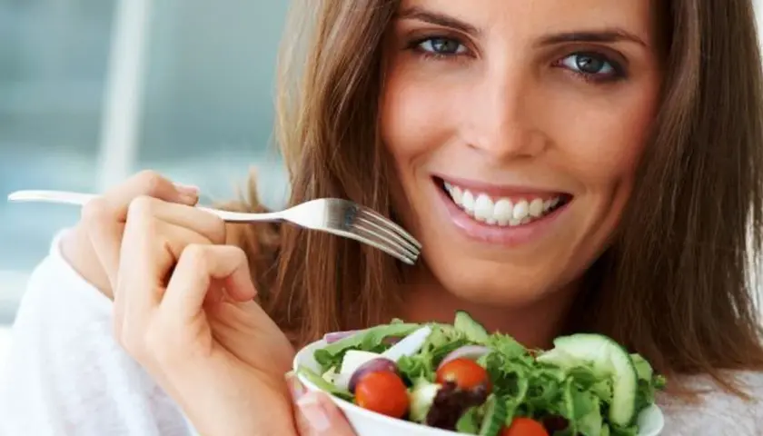 Uśmiechnięta kobieta z apetytem je sałatkę, ciesząc się smakami diety 1200 kcal.