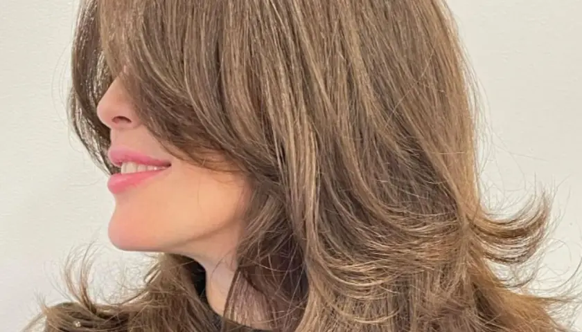 Cabello castaño con un corte mariposa, capas suaves que enmarcan el rostro y dan movimiento.