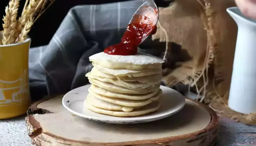 Una cuchara vierte mermelada sobre una pila de tortitas veganas.
