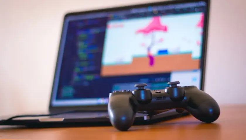 Kontroler PS4 leży przed laptopem z kodem i grą. Dowiedz się, jak podłączyć PS4 do laptopa, by grać na większym ekranie.