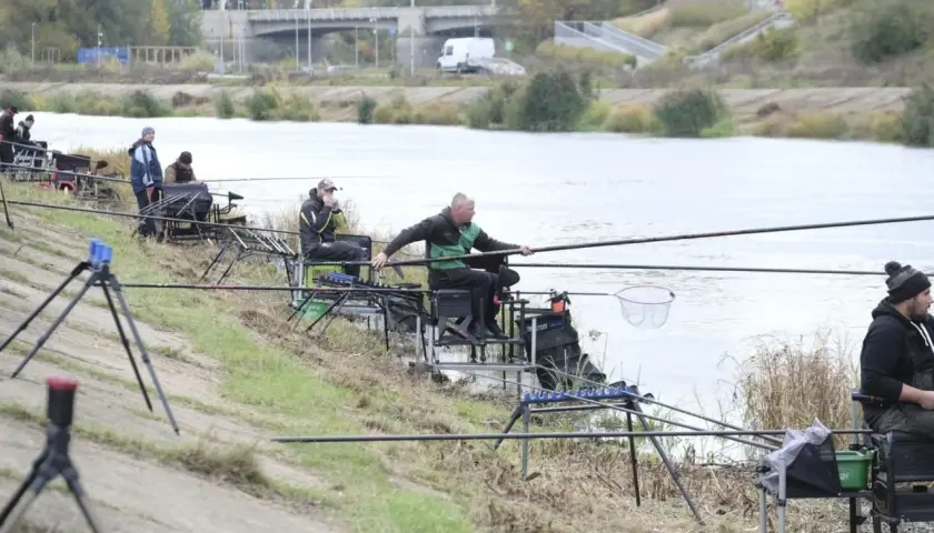 Wędkarze siedzą nad rzeką, łowiąc ryby.