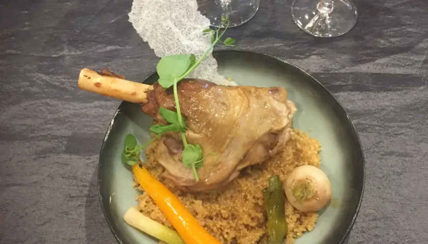 Souris d'agneau braisée au vin, servie sur un lit de couscous avec carottes et navet. Un plat savoureux et réconfortant.