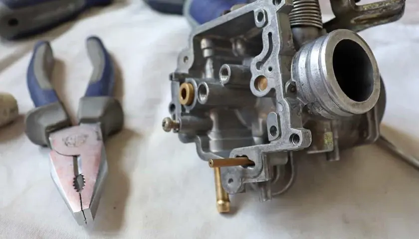 Carburatore smontato, pinze e cacciaviti pronti per la pulizia. Potrebbe essere un modo per risolvere i sintomi di un carburatore sporco.