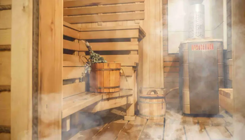 Drewniana sauna z piecem i wiaderkiem z miotełką. Idealne miejsce, by poczuć ciepło i relaks, jakbyś sam wiedział, jak zbudować saunę.