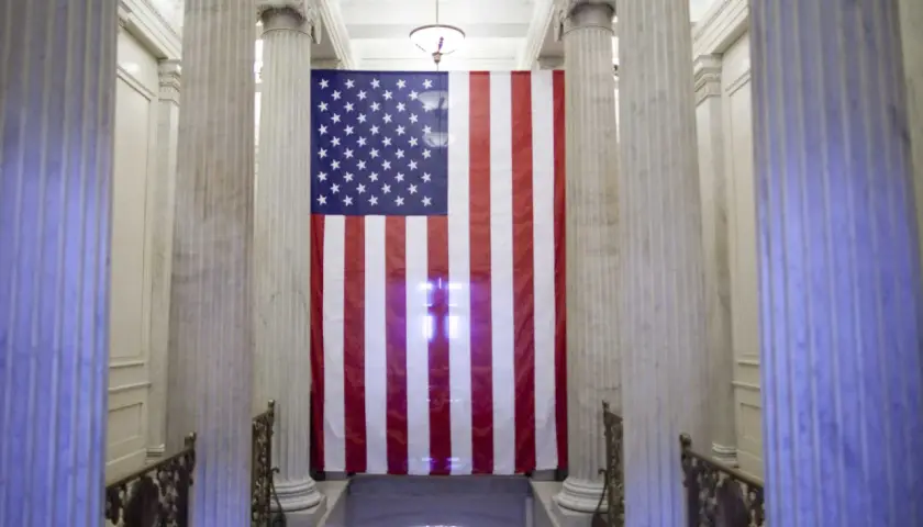 Wielka flaga USA wisi między marmurowymi kolumnami. Czy USA to stany zjednoczone? Tak, to symbol tego kraju.