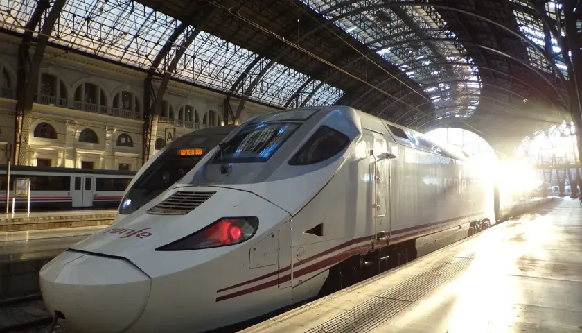 Nowoczesny pociąg Renfe na dworcu, gotowy do podróży z imponującą **tgv prędkość**. Słońce przebija się przez szklany dach.