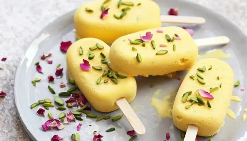 Quatre glaces jaunes, garnies de pistaches et de pétales de rose, sur une assiette. Un délicieux dessert iranien.