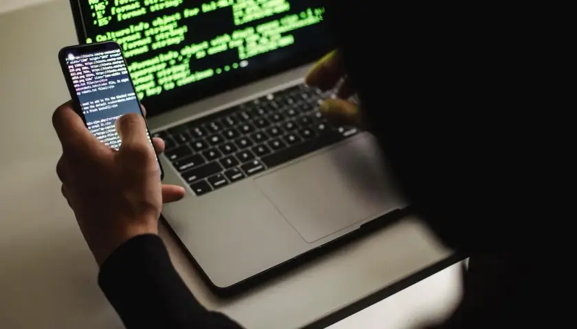 Un développeur web, définition : une personne manipulant du code sur un smartphone et un ordinateur portable, éclairés par la lueur verte des écrans.