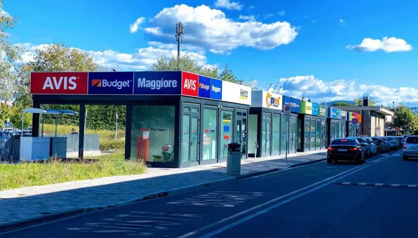 Car rental agencies like Avis, Budget, Maggiore, Hertz, and Europcar line the street, offering options for how to rent a car in Florence, Italy.