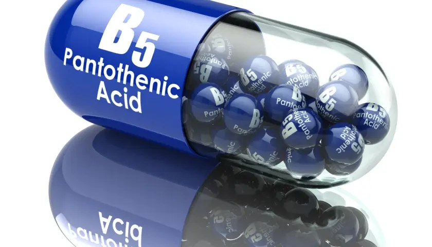 Niebieska kapsułka z napisem "B5 Pantothenic Acid" zawiera małe kuleczki z tym samym oznaczeniem. Witamina B5 w pigułce.