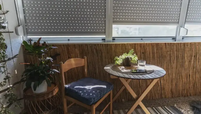 Przytulna loggia z balkonem, gdzie stoi drewniane krzesło z poduszką, okrągły stolik z napojem i roślinami.