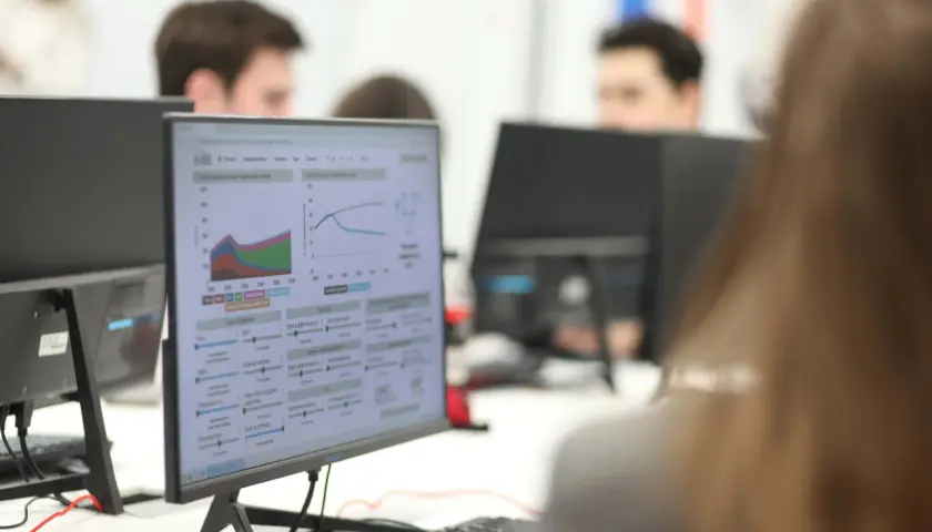 Studenci ekonomiczne analizują wykresy i dane na monitorach, pracując nad projektami.