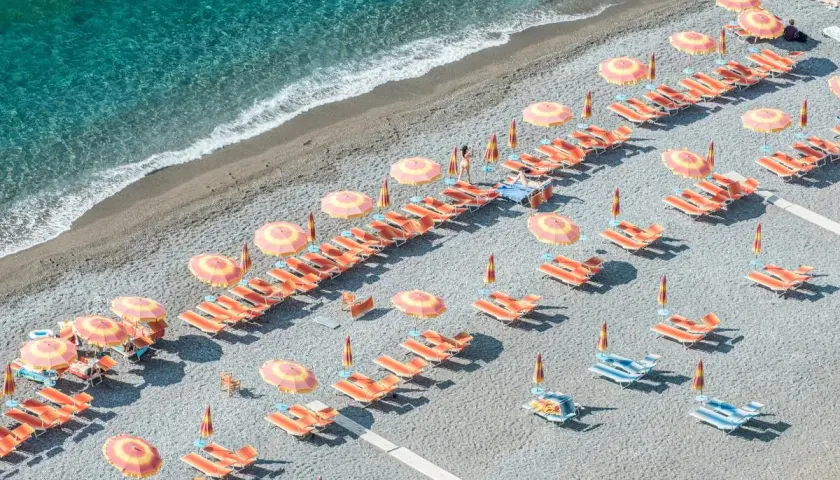 Lignes d'orange vif et de parasols colorés sur une plage de galets, une invitation à la détente. Destination Italie plage.