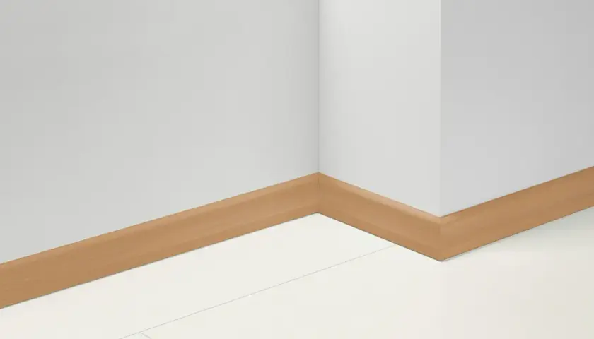 Angolo di una stanza con battiscopa in PVC effetto legno. Impara come tagliare battiscopa PVC per un'installazione perfetta.