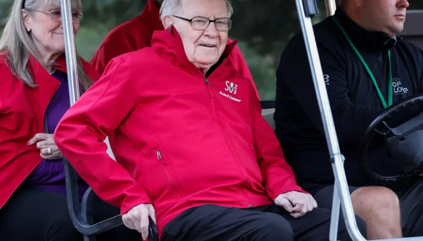 Warren Buffett w czerwonej kurtce z logo Allen & Company, siedzi w golfowym wózku.