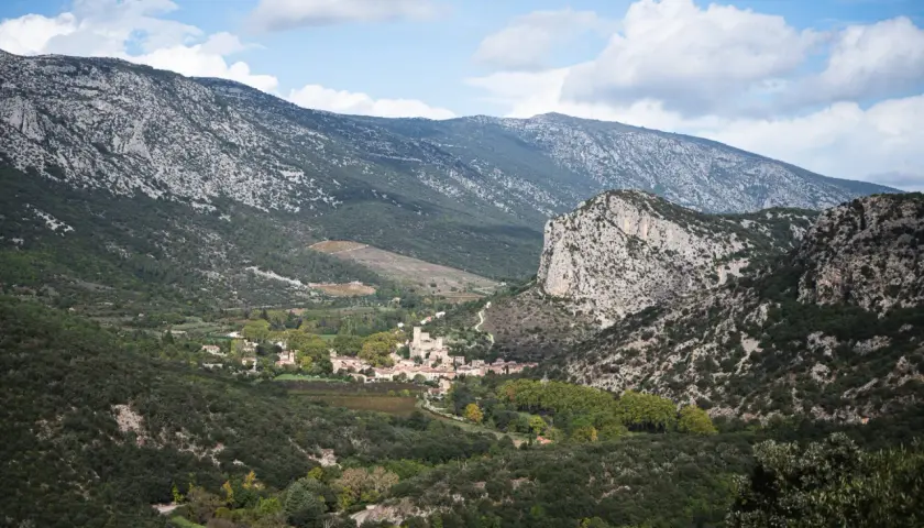 Vue panoramique sur le village de Saint-Guilhem-le-Désert, niché au creux de montagnes rocheuses. Un paysage idéal pour déguster un vin rouge local.