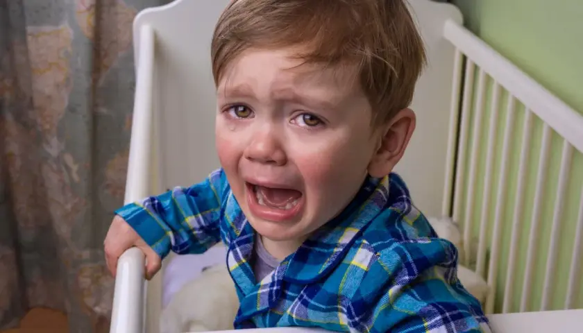 Un niño pequeño con pijama a cuadros llora desconsoladamente en su cuna. Sus ojos están llenos de lágrimas y su boca abierta en un grito.