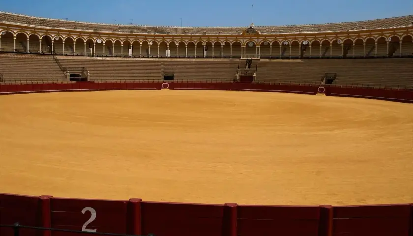 Arena vacía de una de las plazas de primera en España, con gradas y el ruedo de arena dorada bajo un cielo azul.