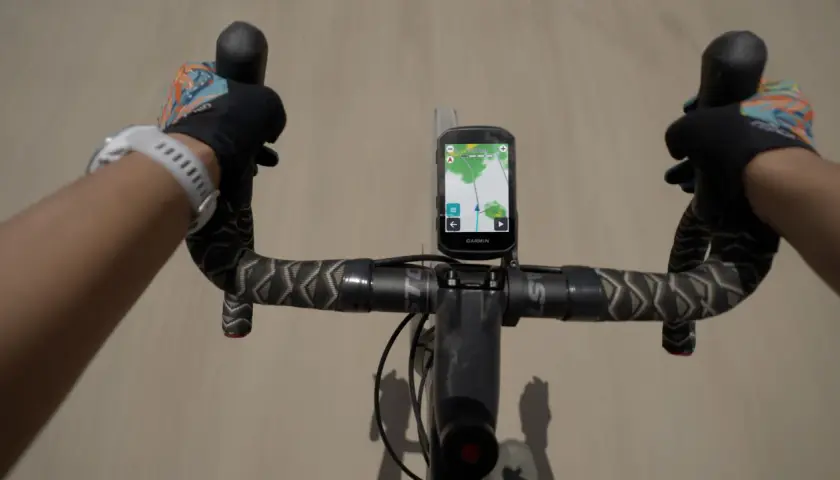 Rowerzysta z rękami w rękawiczkach na kierownicy, na której zamontowany jest Garmin z mapą. Zastanawiasz się, jaki Garmin wybrać?