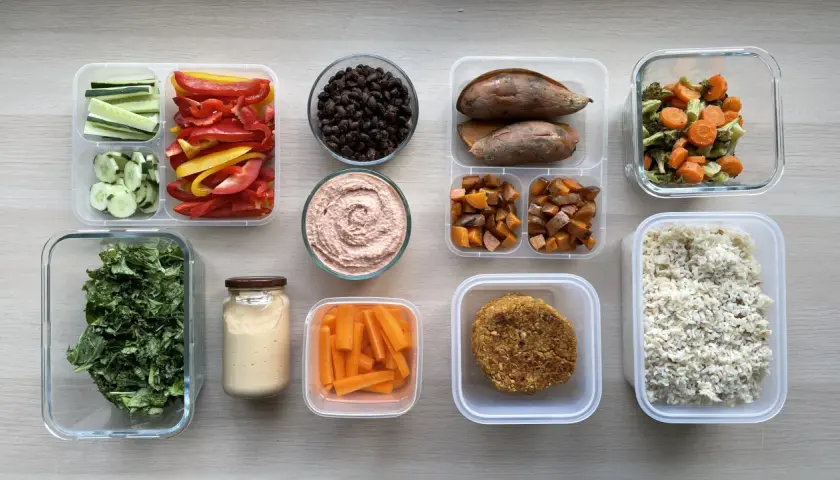 Healthy Japanese bento box ideas for adults: rice, veggie patties, roasted sweet potatoes, carrots, hummus, black beans, and fresh greens.