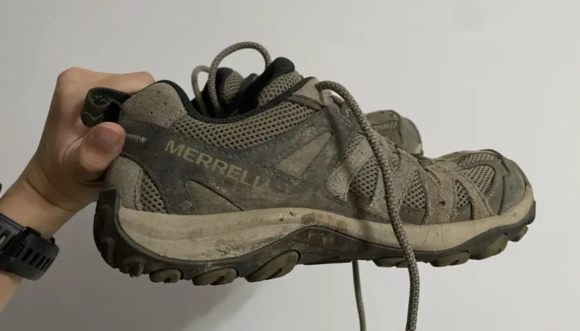 A muddy Merrell hiking shoe is held up, showing its worn tread. This image might inspire ideas on how to rough up the bottom of slippery shoes for better grip.