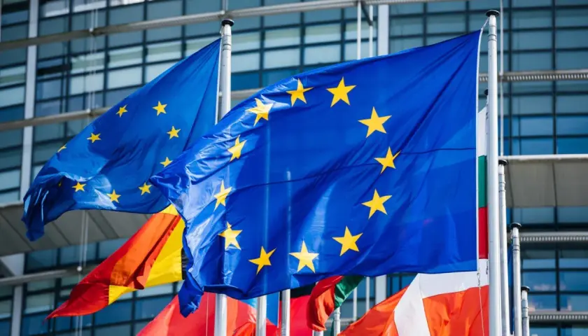 Flagi Unii Europejskiej powiewają przed nowoczesnym budynkiem, symbolizując jedność i współpracę krajów członkowskich.