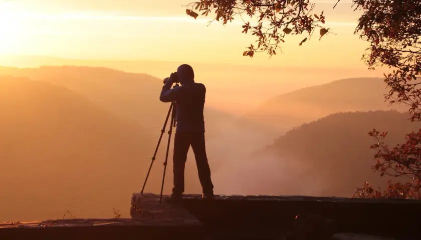 Fotograf na skale, wykonujący pomiar światła o wschodzie słońca. Mgła spowija doliny, tworząc malowniczy krajobraz.